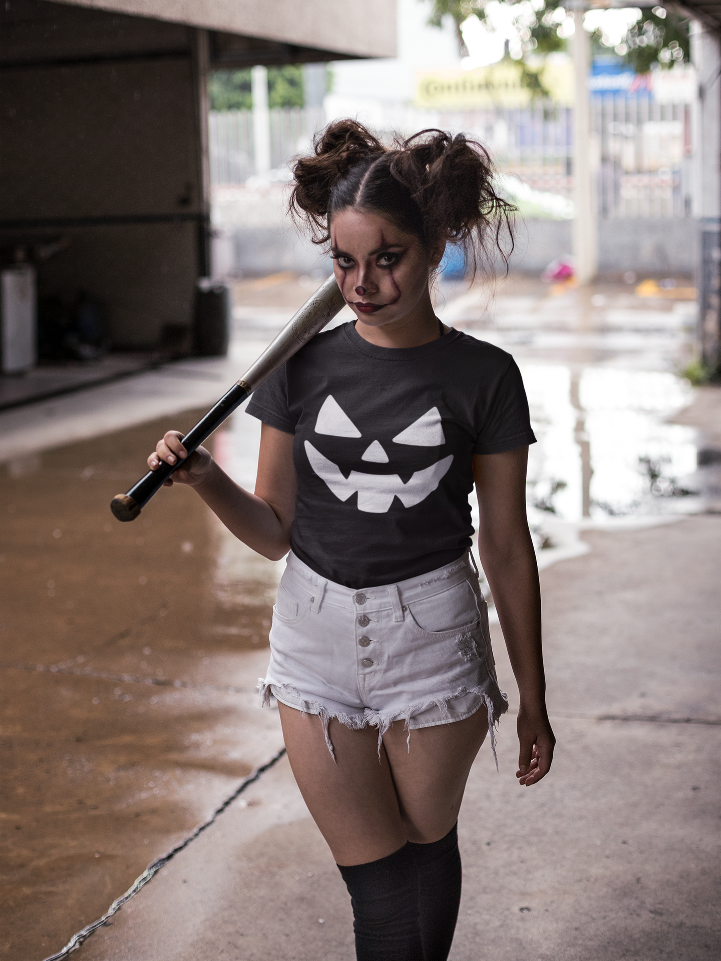 Person wearing a black t-shirt with a white pumpkin design, holding a baseball bat, in an outdoor setting.