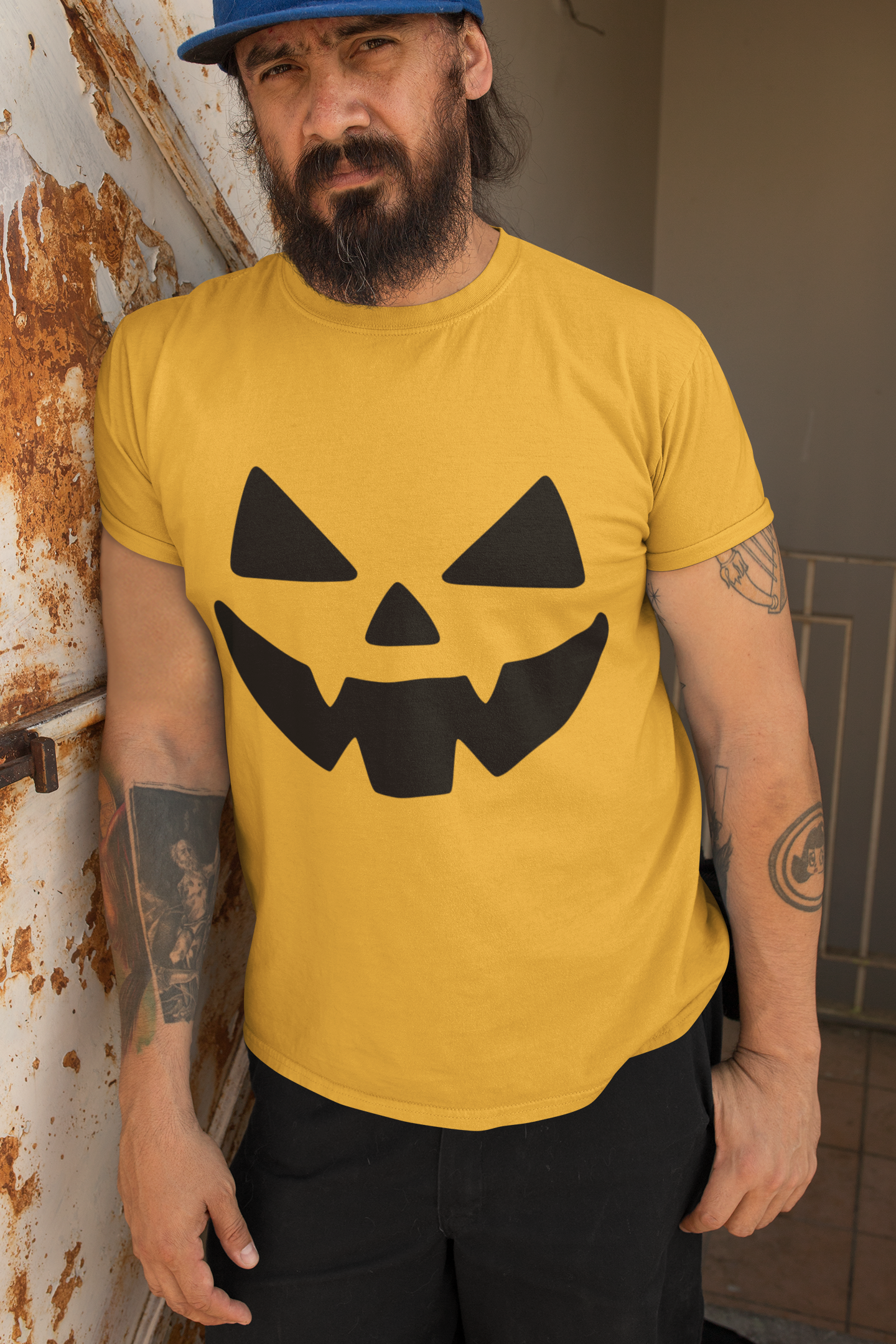 Man wearing a yellow t-shirt with a black jack-o'-lantern face design, standing against a rusty metal wall.