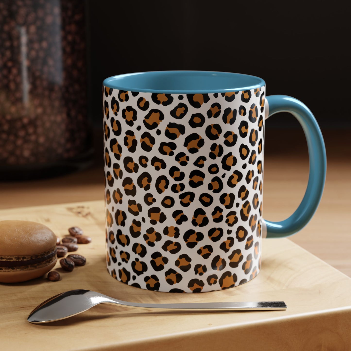 Mug with leopard print pattern on a wooden surface with coffee beans and a spoon.