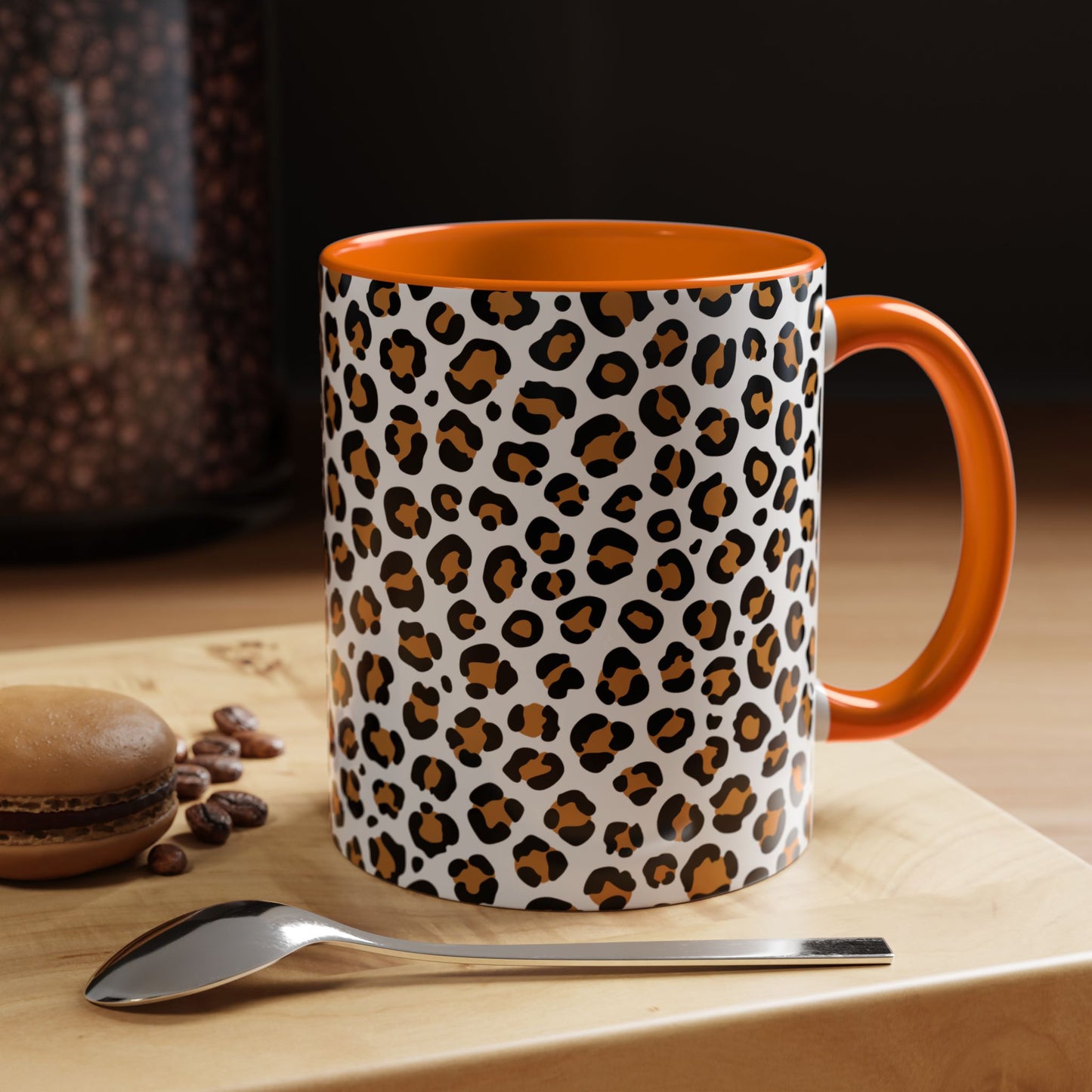 Leopard print mug with orange interior and handle on a wooden surface with coffee beans and a macaron.