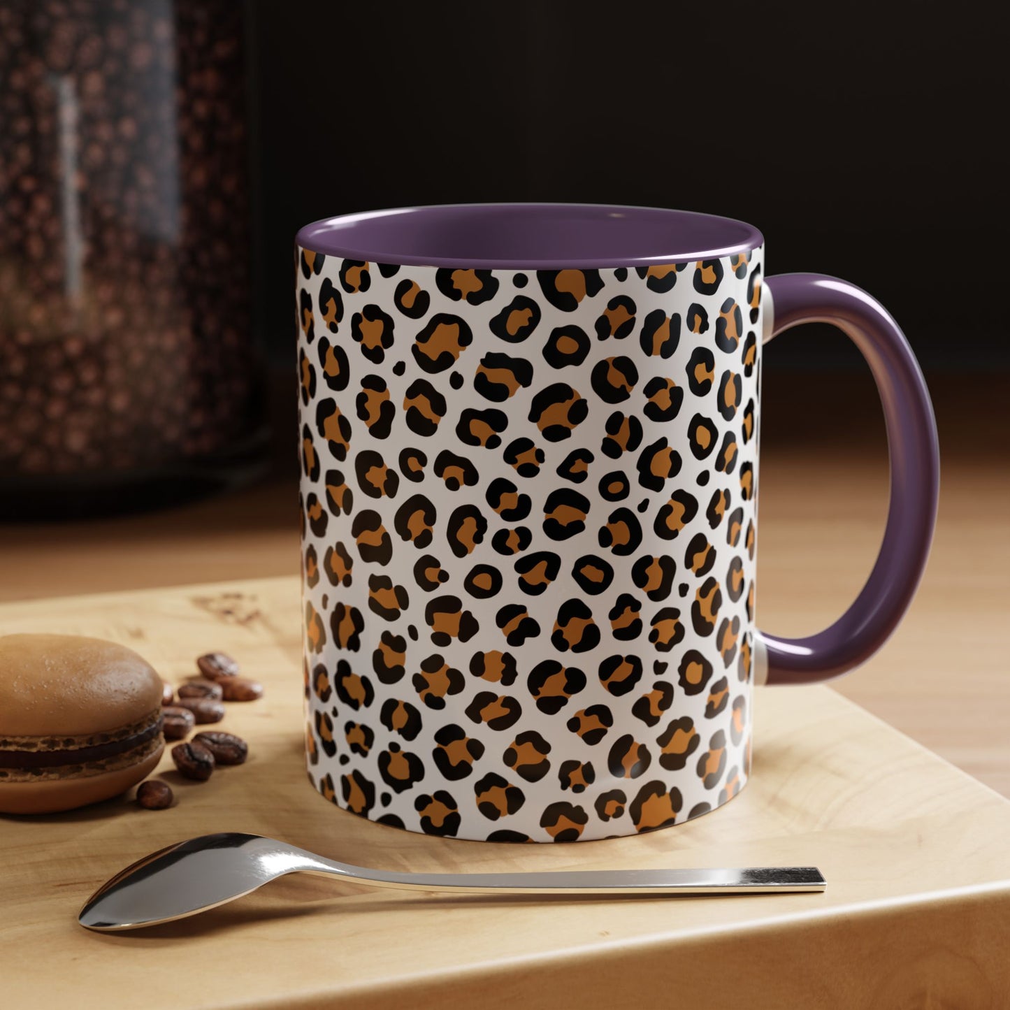 Leopard print mug with purple interior and handle on a wooden surface with coffee beans and a spoon.