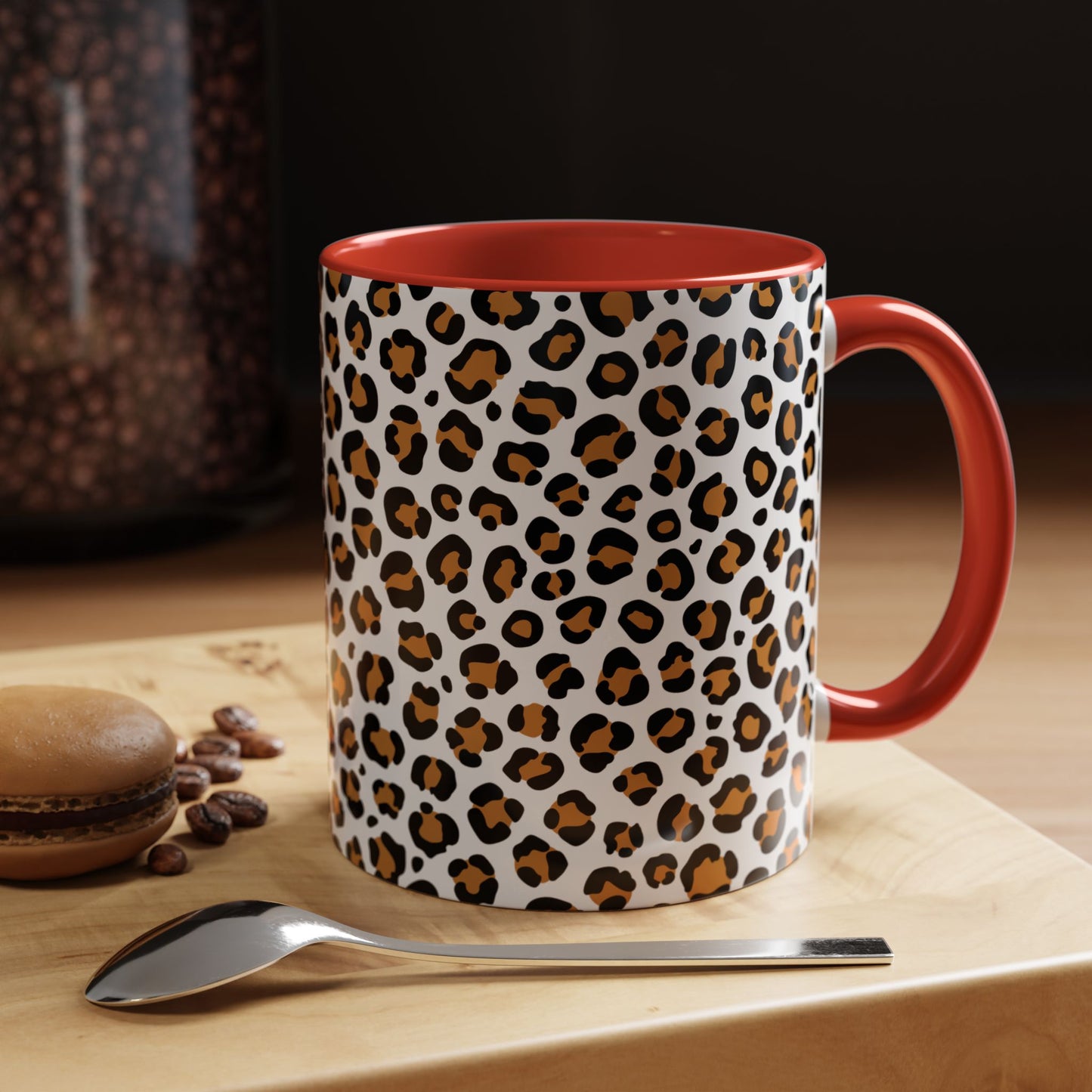 Leopard print mug with red interior and handle on a wooden surface with coffee beans and a spoon.