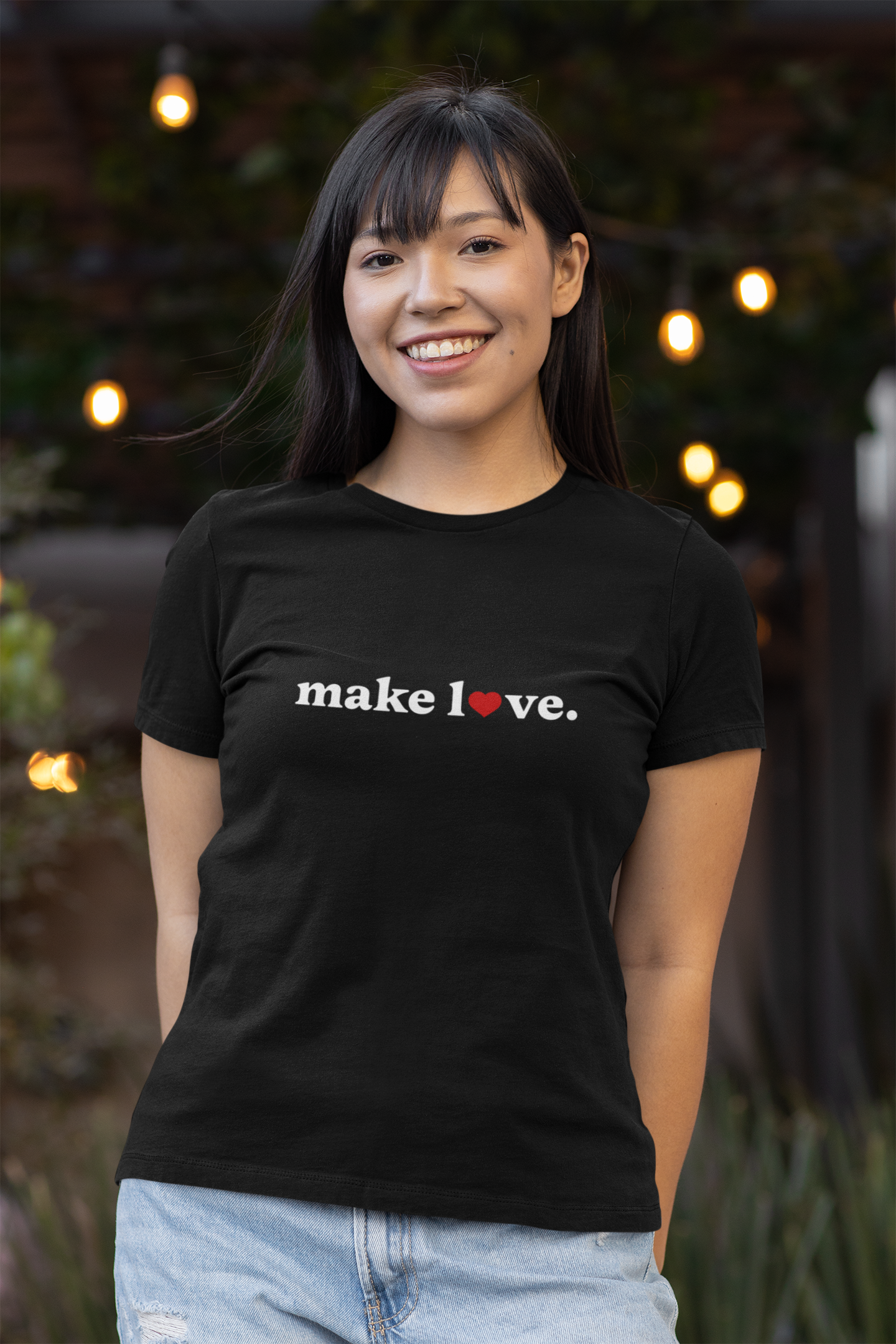 Woman wearing a black t-shirt with 'make love' text, standing outdoors with lights in the background.