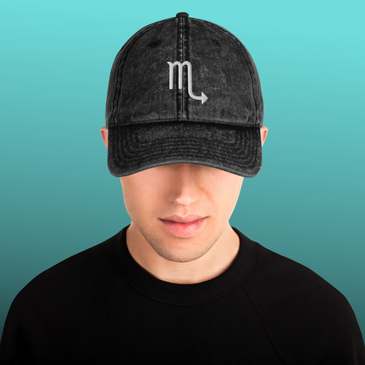 Person wearing a black cap with a white Scorpio symbol on a teal background