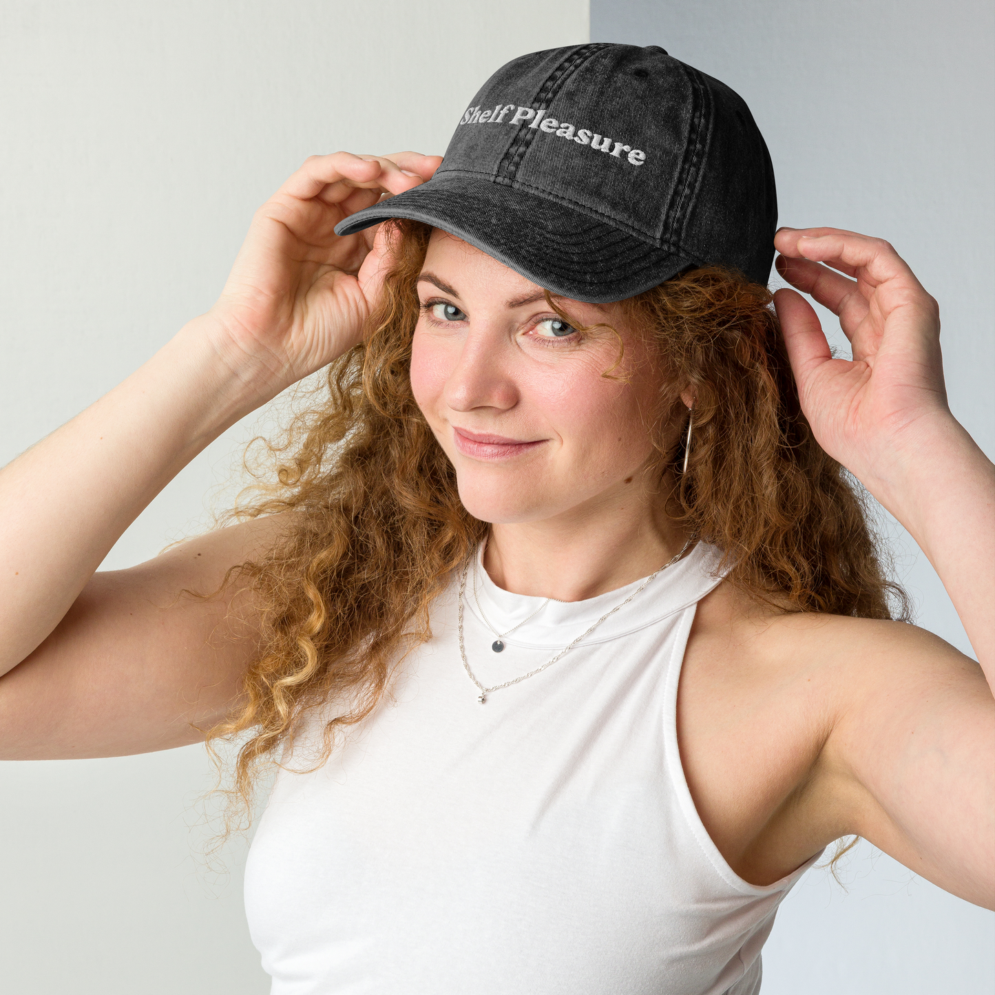 Woman wearing a black cap with 'Self Pleasure' text, posing against a light gray background