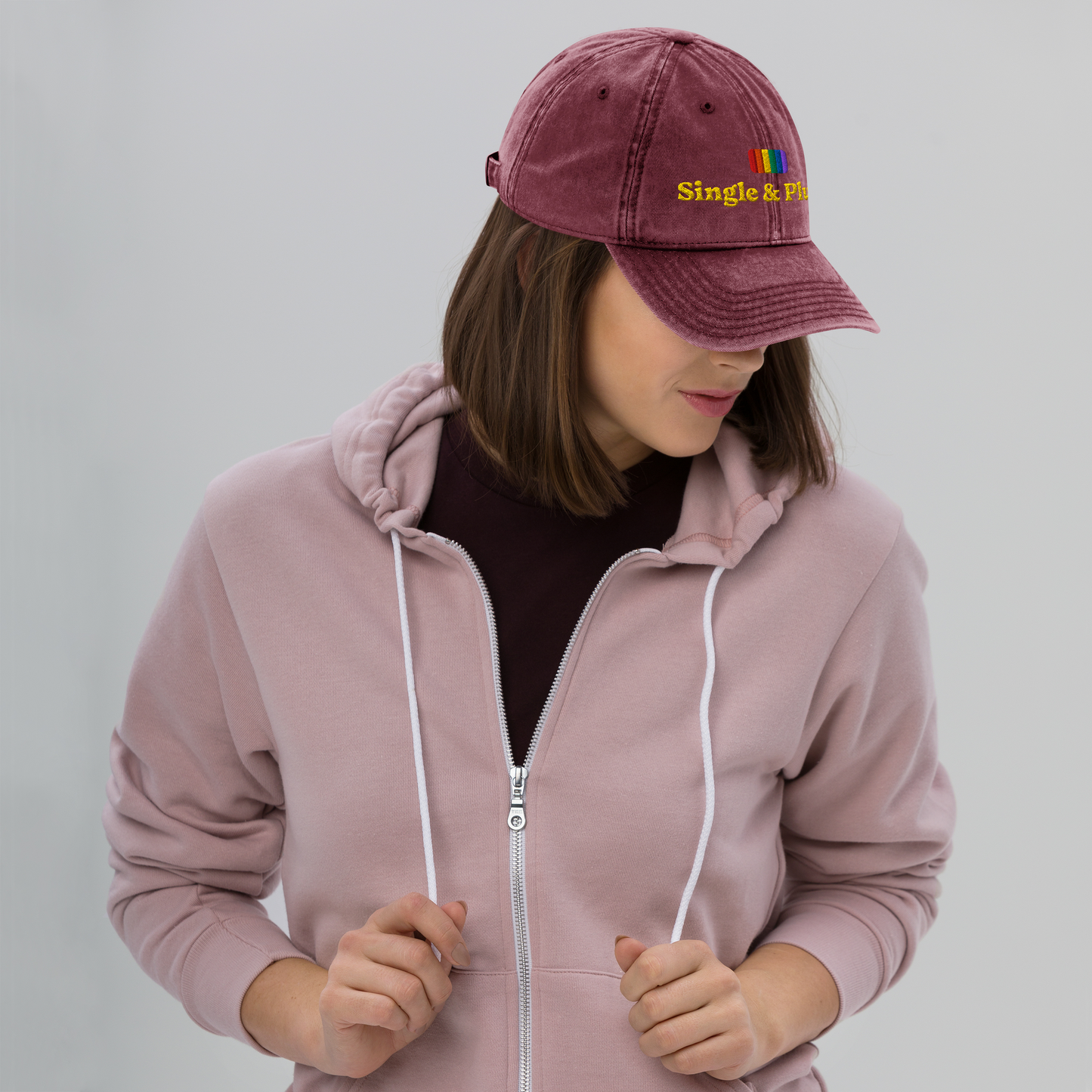 Person wearing a pink hoodie and maroon cap with 'Single & Plural' text on a gray background