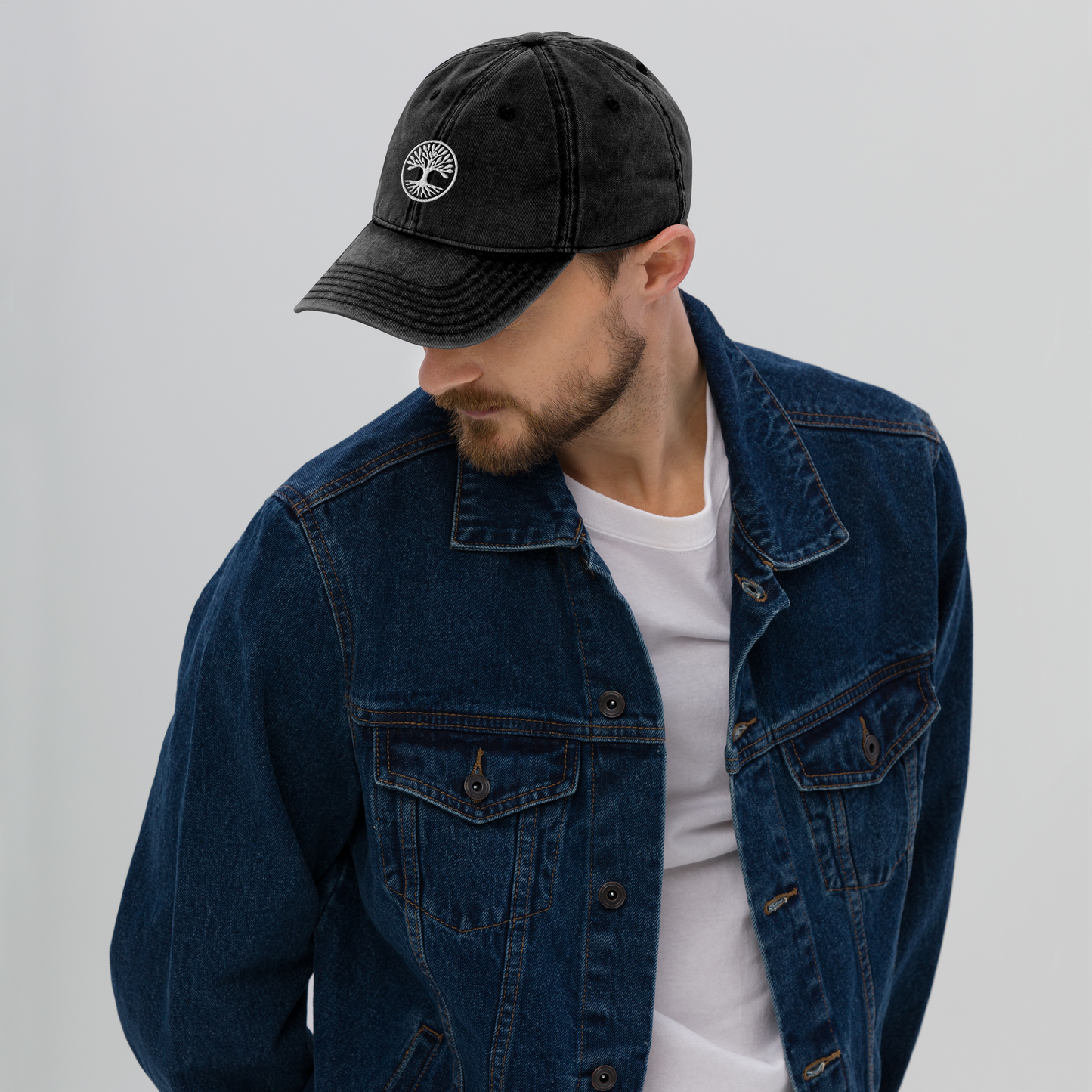 Man wearing a black cap with a logo and a blue denim jacket on a light gray background