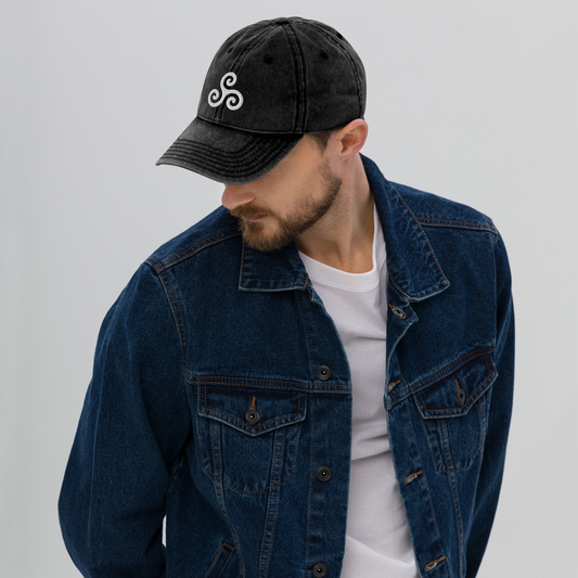 Man wearing a black cap with a logo and a blue denim jacket on a light gray background