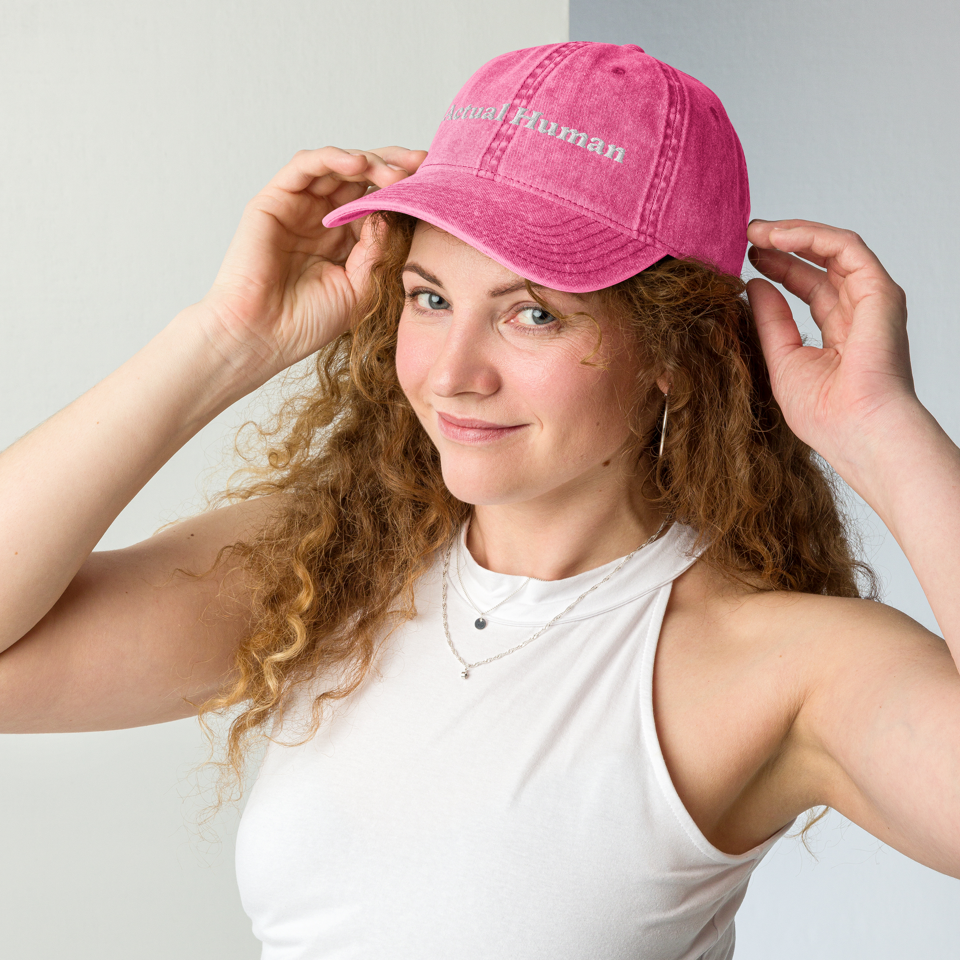 Woman wearing a pink cap with text, posing against a plain background