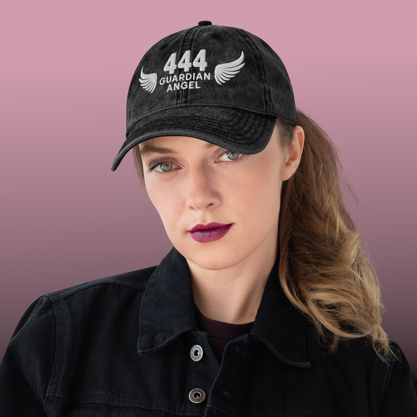 Person wearing a black cap with '444 Guardian Angel' text against a pink background