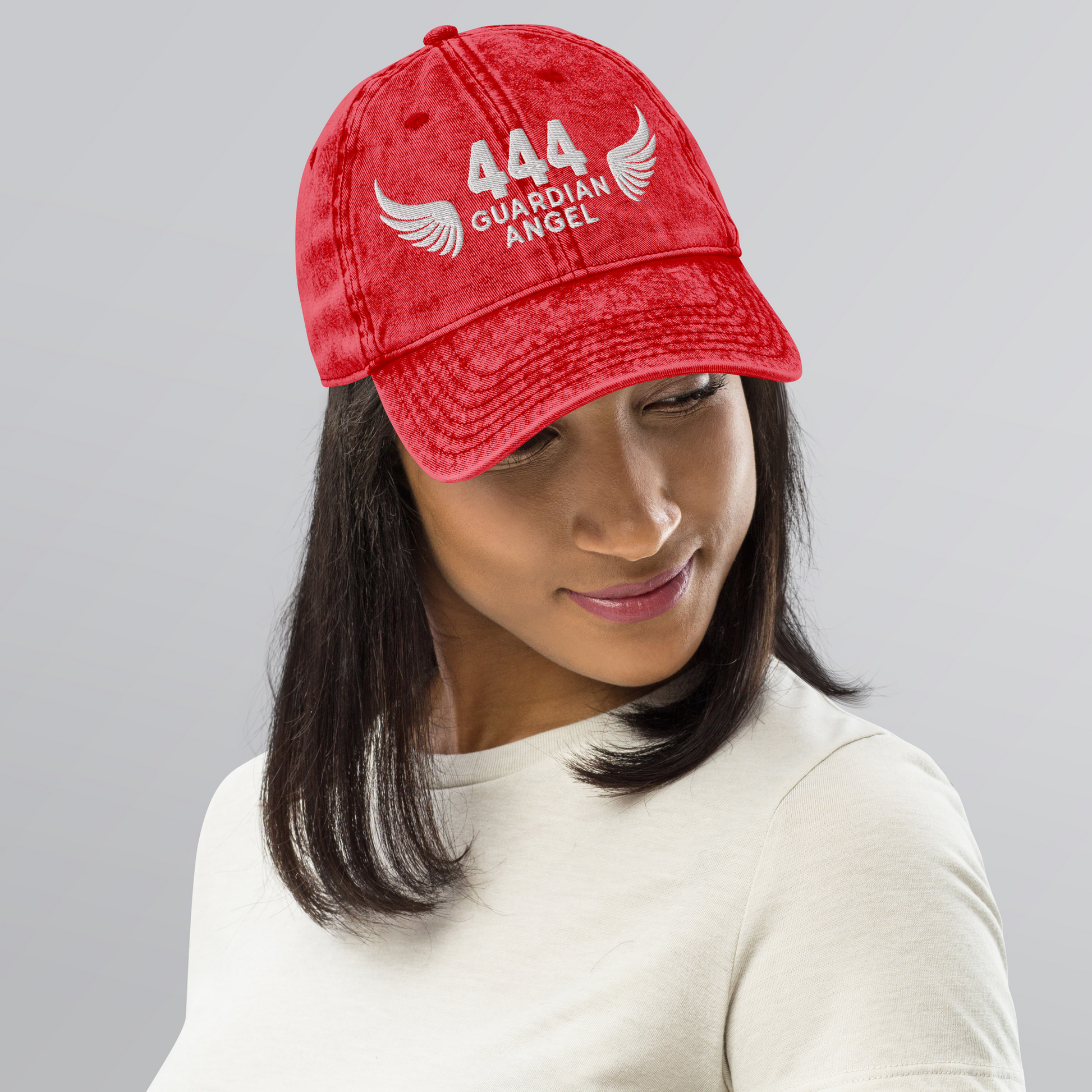 Person wearing a red cap with '444 Guardian Angel' text and wings on a gray background