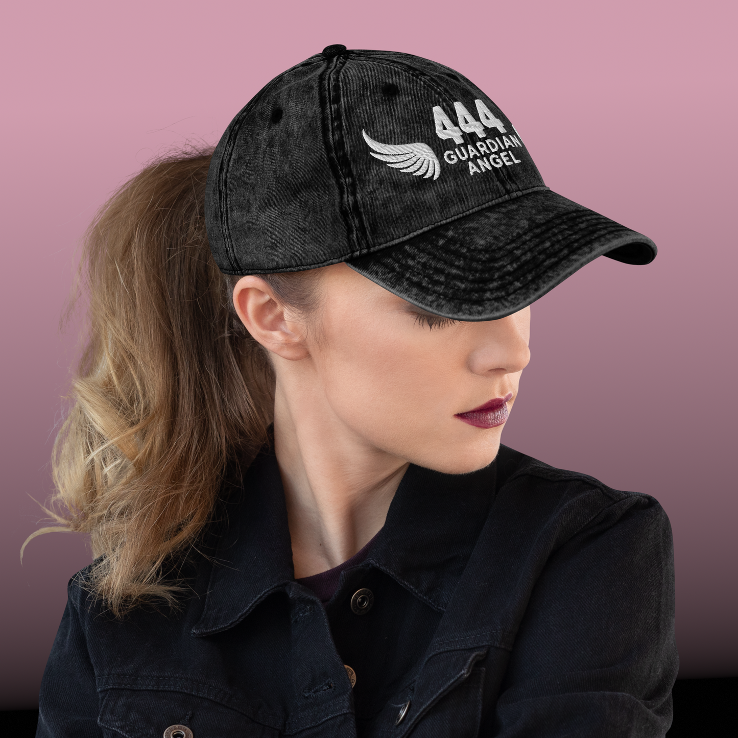 Person wearing a black cap with '444 Guardian Angel' text and logo on a pink background