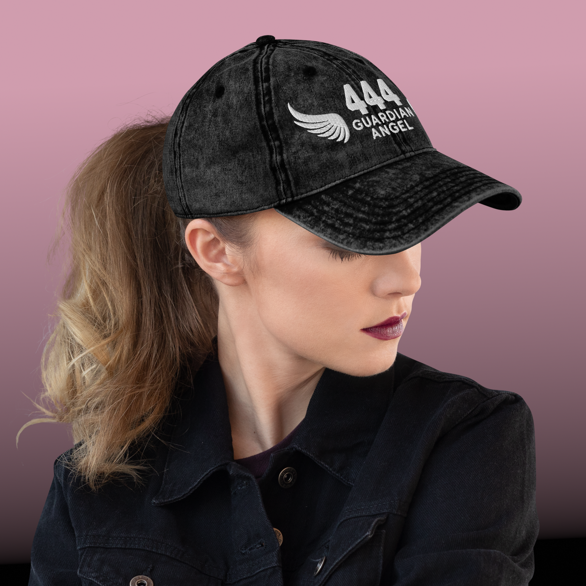 Person wearing a black cap with '444 Guardian Angel' text and logo on a pink background