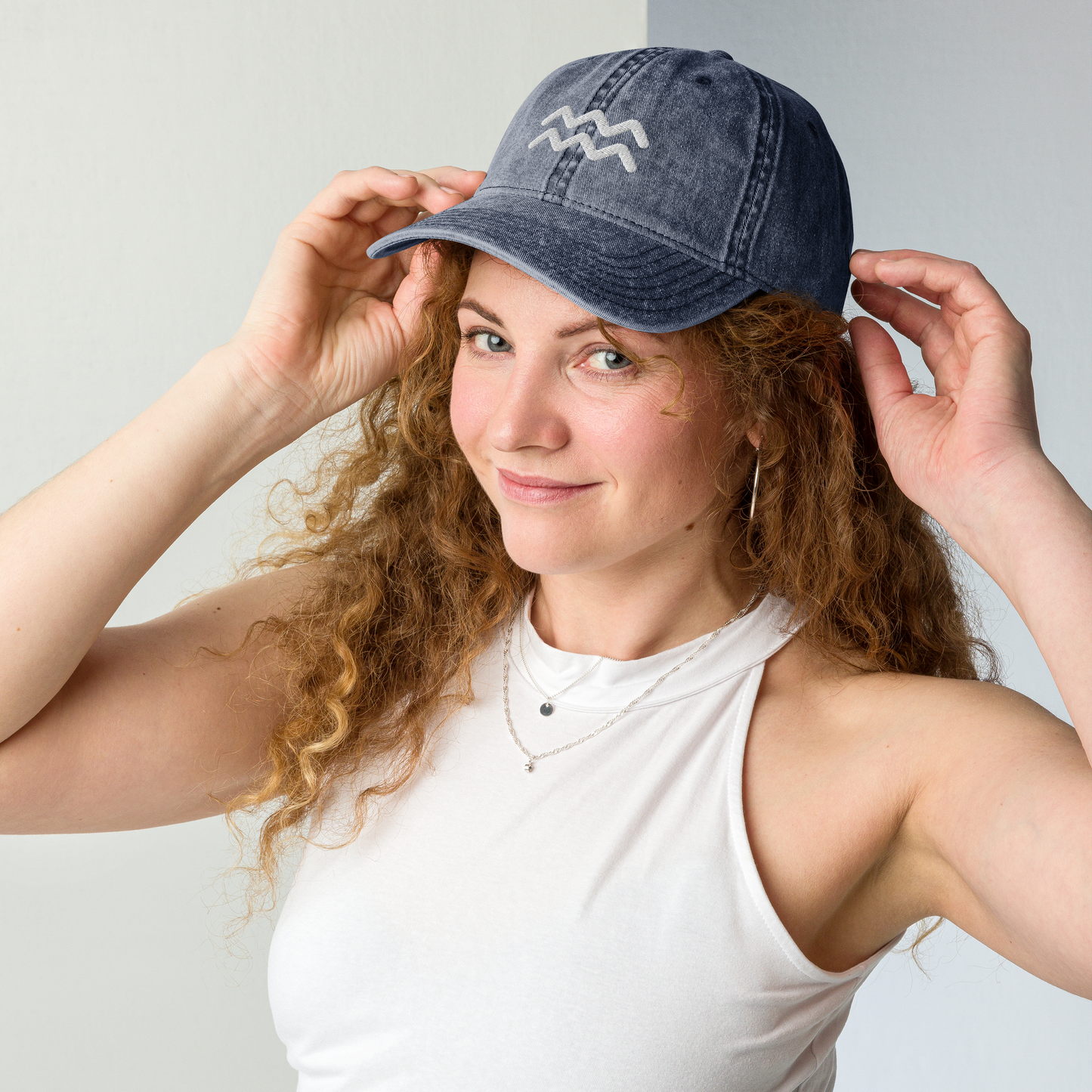 Woman wearing a blue denim cap with an aquarius logo, posing against a light gray background