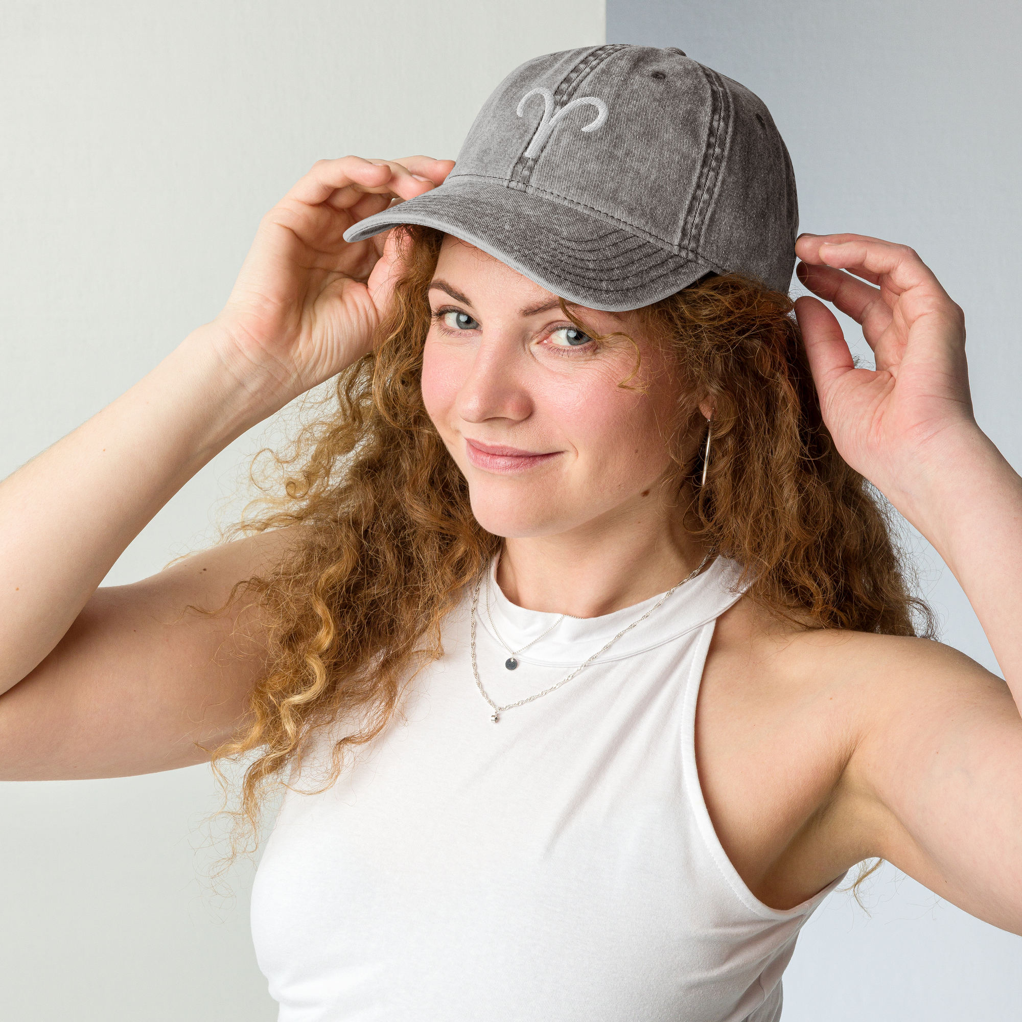 Woman wearing a gray baseball cap with an aries white logo against a light background