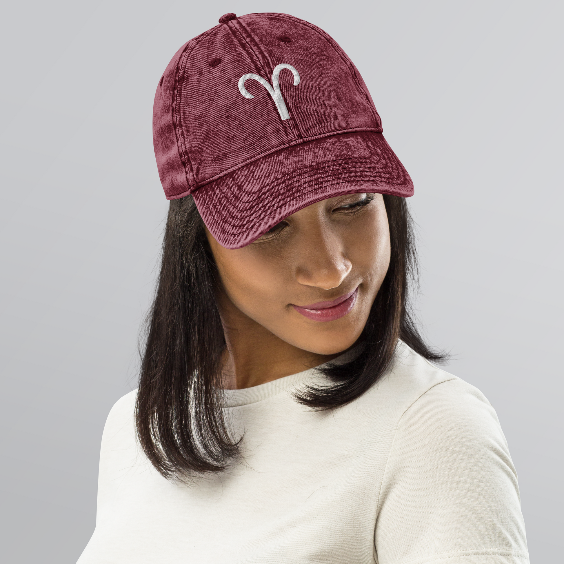 Person wearing a maroon baseball cap with a white aries symbol on a gray background