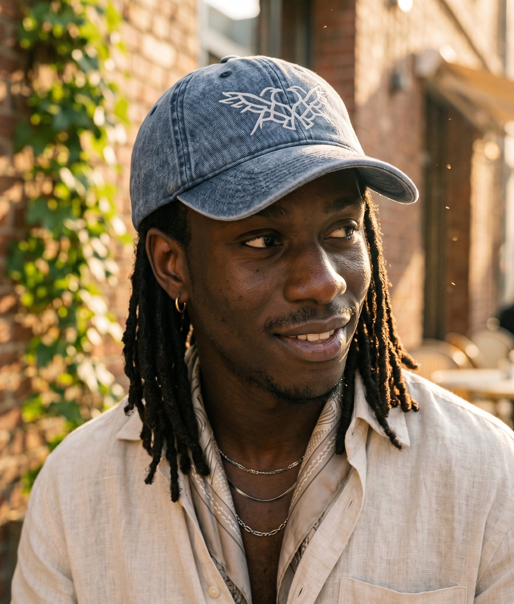 Man wearing a denim cap outdoors with a brick wall and greenery in the background