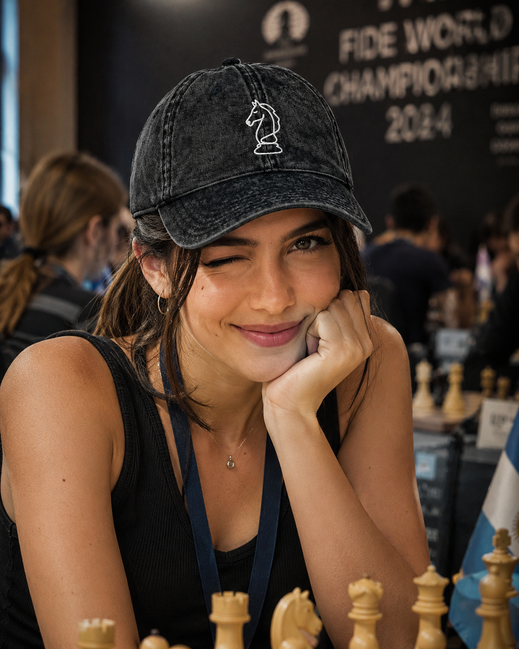 Woman wearing a cap with a chess piece design, sitting at a chessboard during a chess championship event.