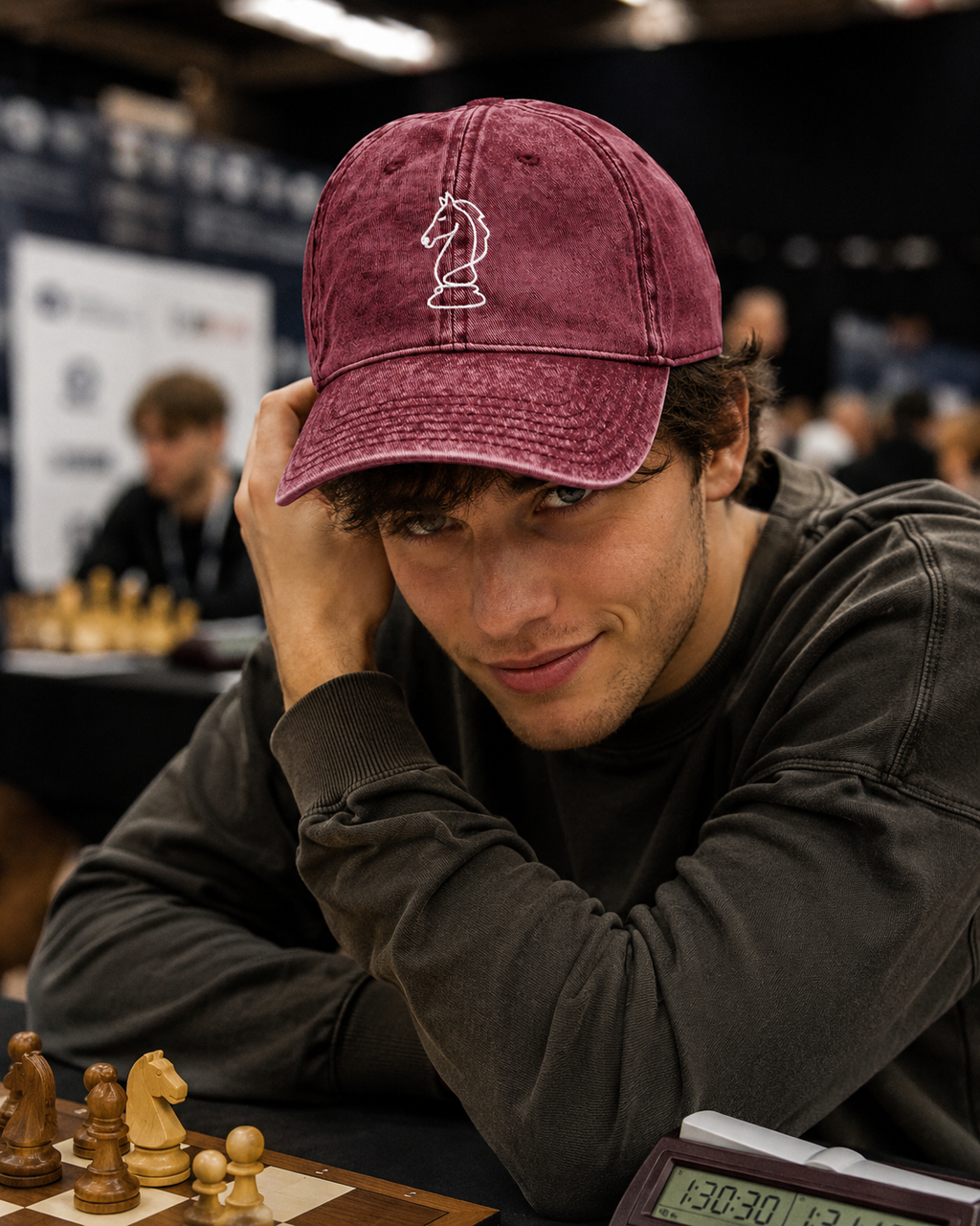 Person wearing a maroon cap with a chess piece design, sitting at a chessboard.