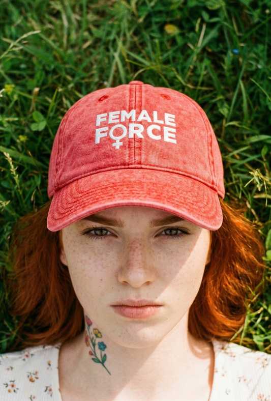 Person wearing a red 'FEMALE FORCE' cap in a grassy field