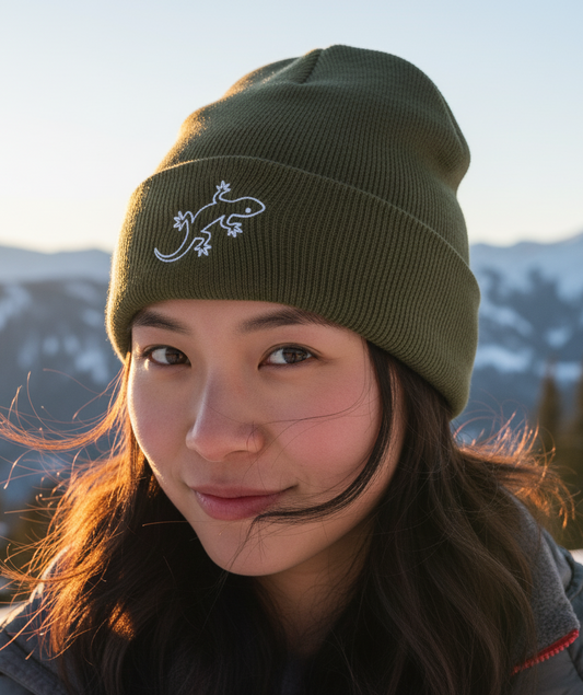 Person wearing a green beanie with a lizard design against a mountainous background