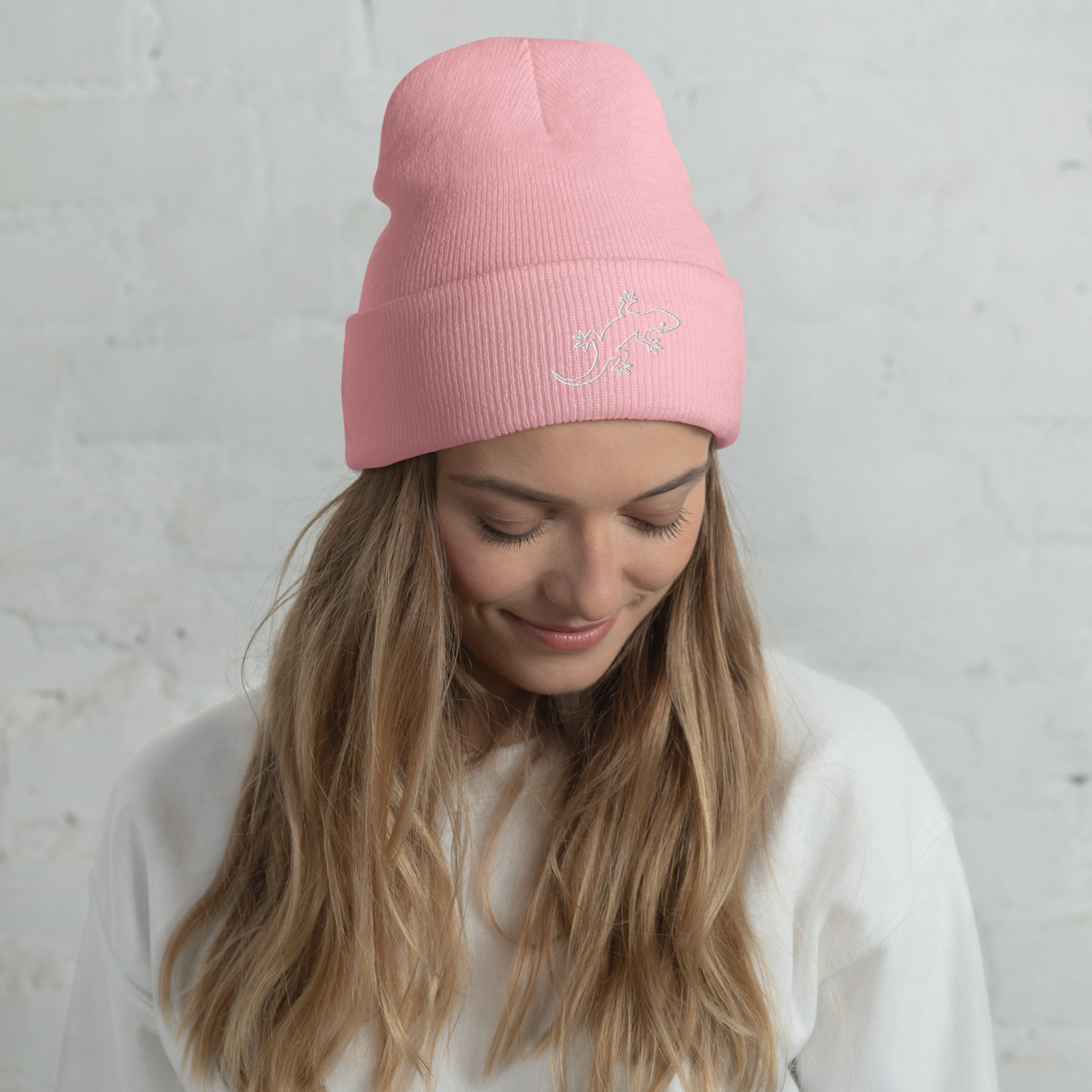 Woman wearing a pink beanie with a gecko logo against a light gray background