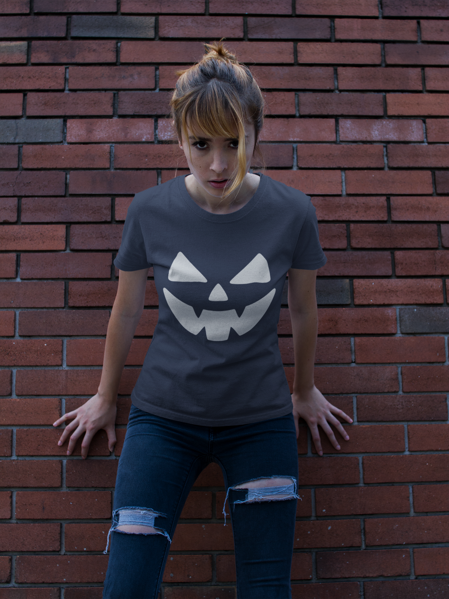 Person wearing a t-shirt with a jack-o'-lantern face design against a brick wall.