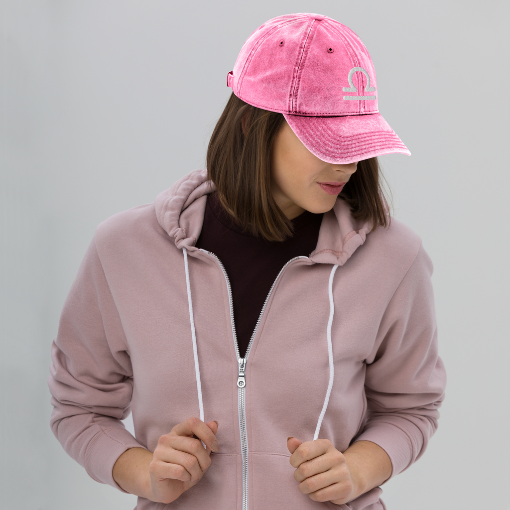 Person wearing a pink hoodie and matching cap with a libra sign on a gray background