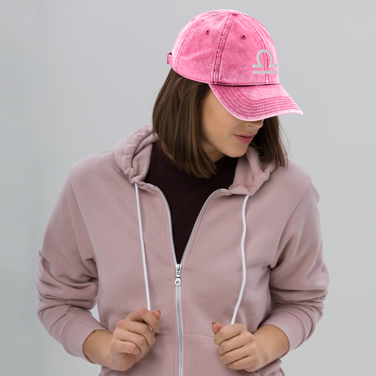 Person wearing a pink hoodie and matching cap with a libra sign on a gray background
