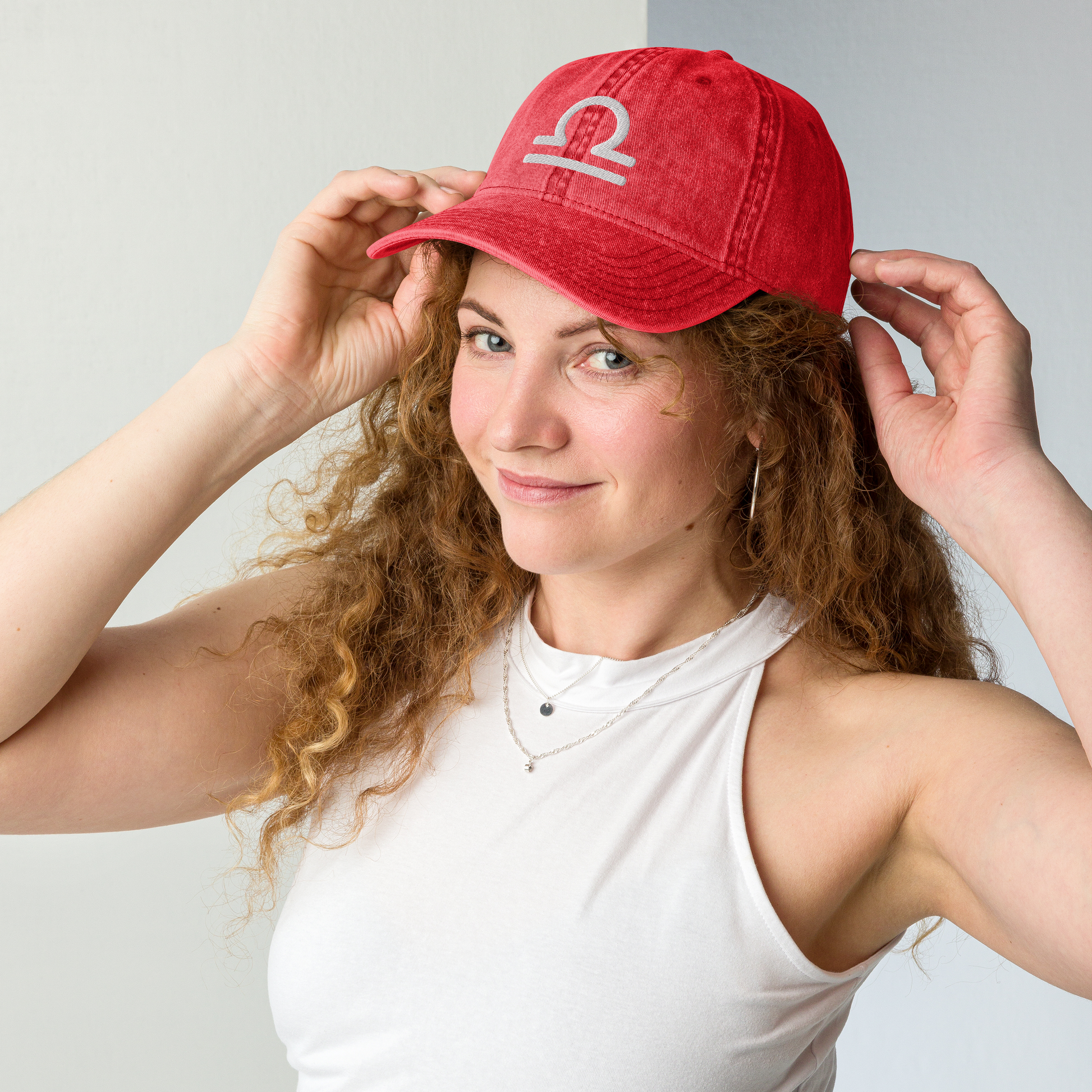 Woman wearing a red cap with a libra logo on a plain background