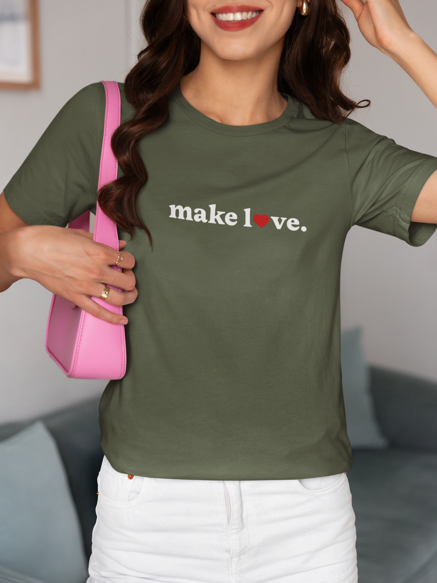 Person wearing a green t-shirt with 'make love' text, holding a pink bag indoors.