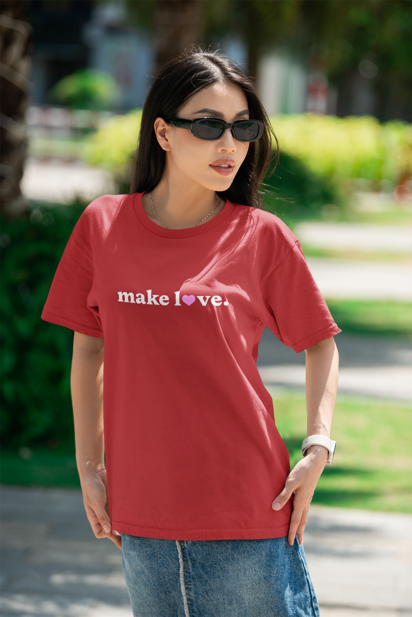 Woman wearing a red t-shirt with 'make love' text outdoors.