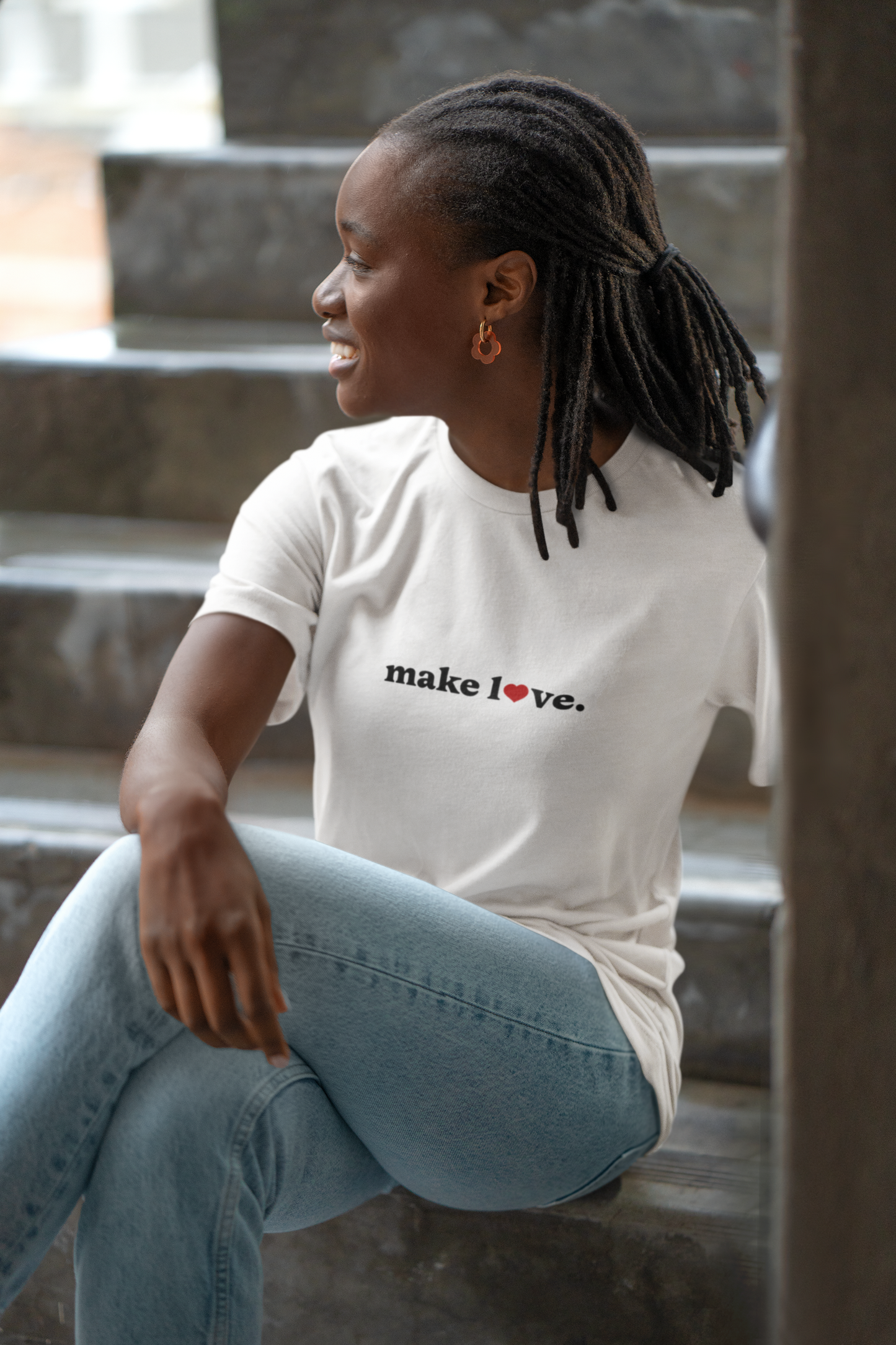 Person wearing a white t-shirt with 'make love' text sitting on steps.