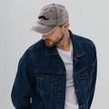 Man wearing a denim jacket and cap with a mustache design on a plain background