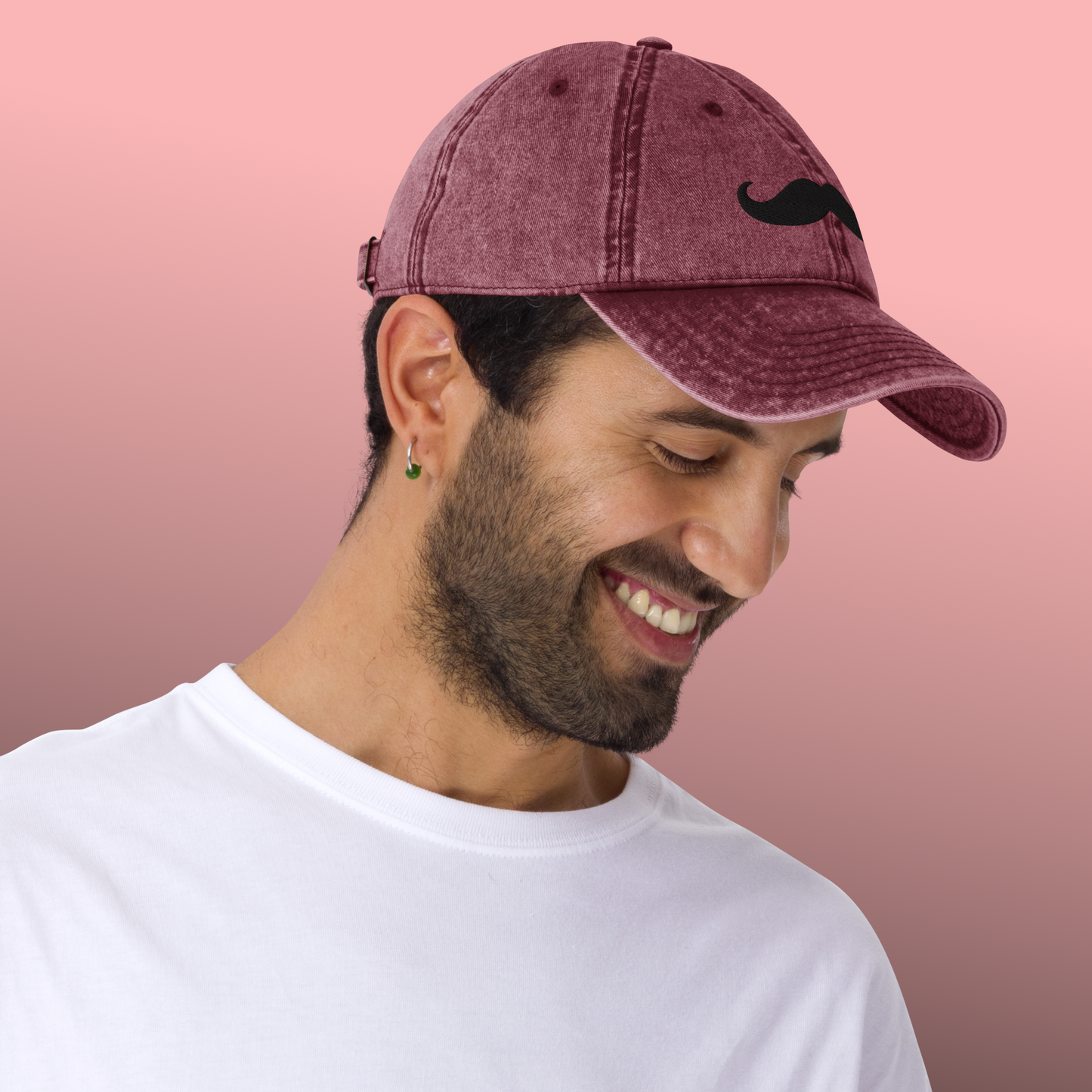 Man wearing a maroon cap with a mustache design on a pink background