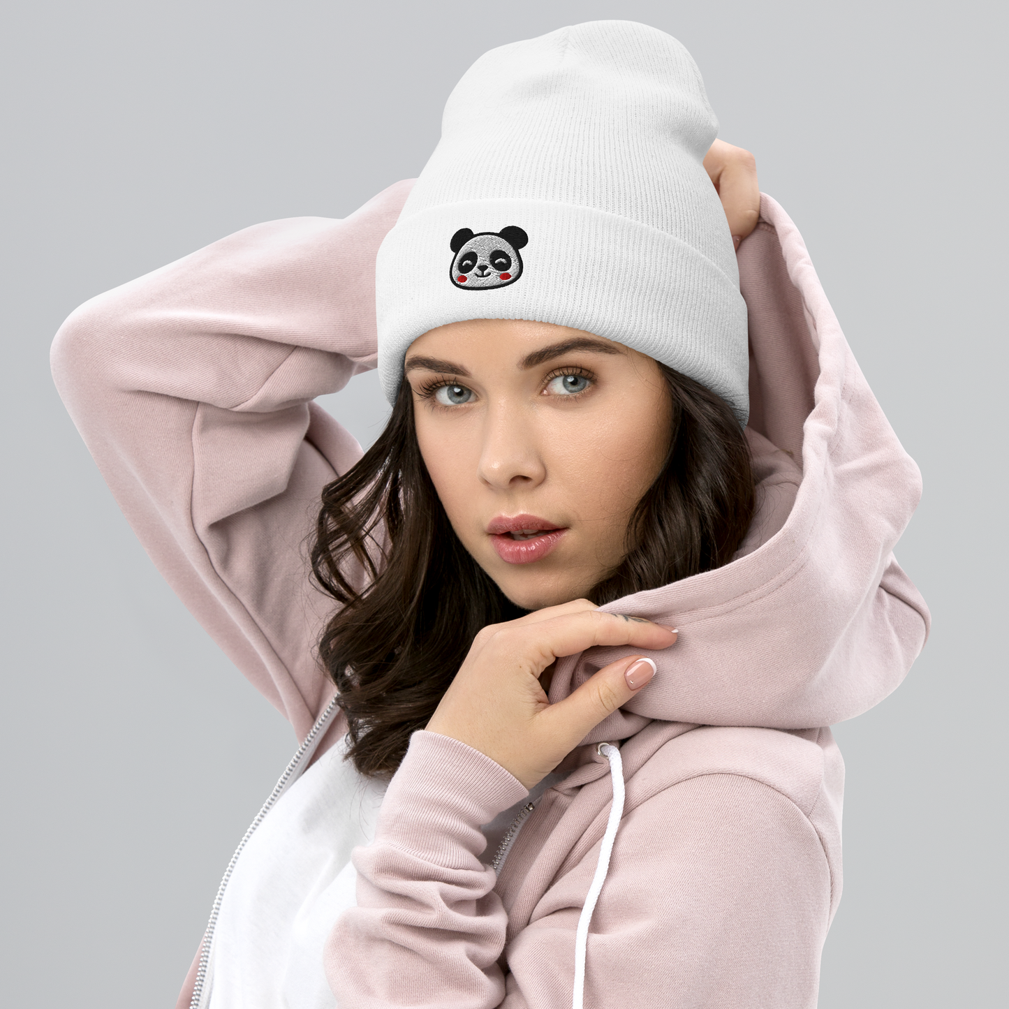 Woman wearing a light pink hoodie and white beanie with a panda design on a gray background