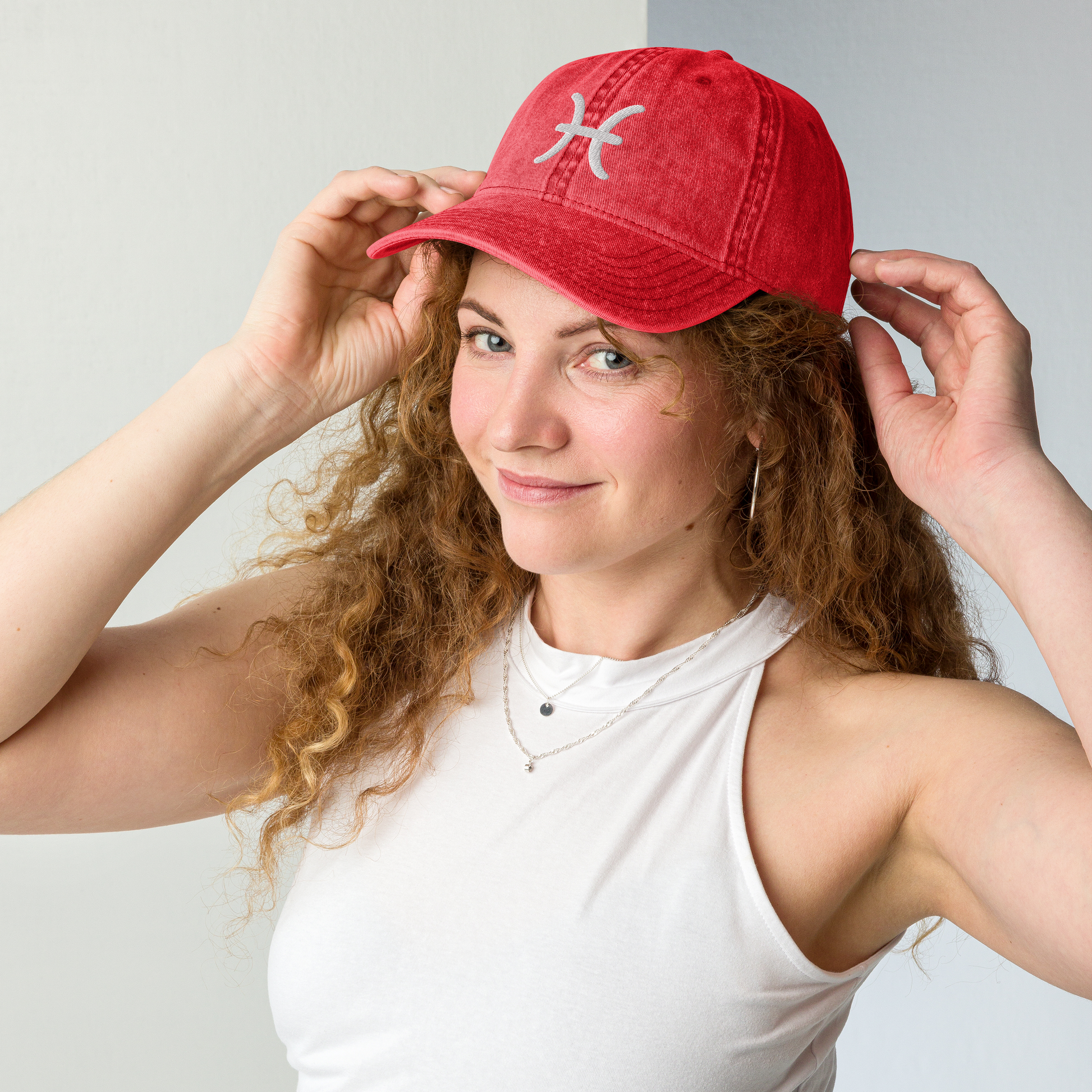 Woman wearing a red cap with a white pisces logo against a plain background