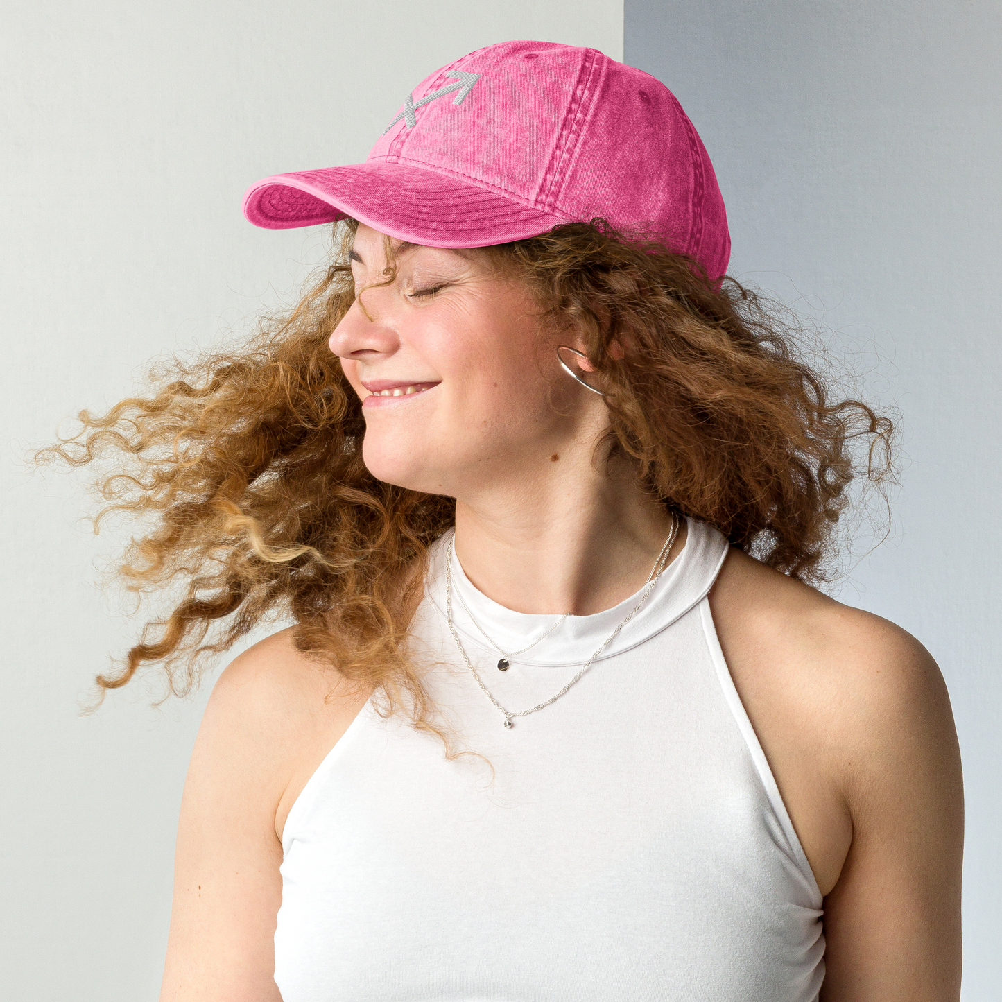 Woman wearing a pink cap and white tank top against a light gray background