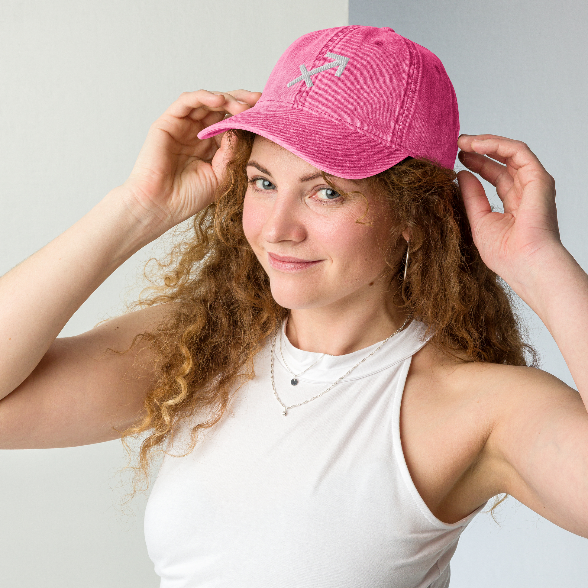 Woman wearing a pink cap with a Sagittarius logo on a light gray background