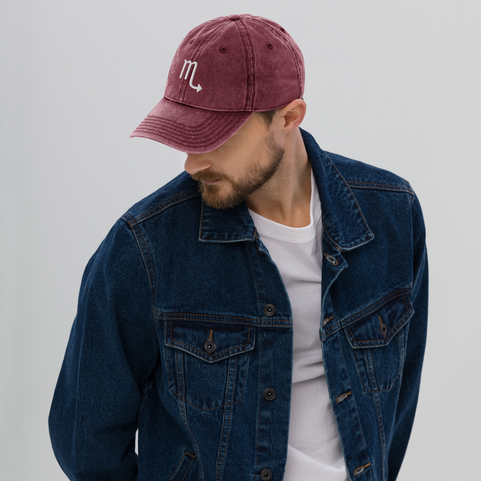 Man wearing a denim jacket and maroon cap with a white logo on a light gray background