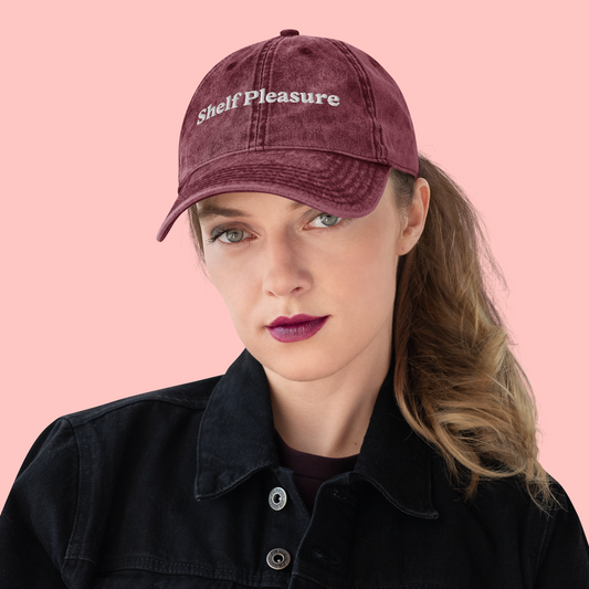 Person wearing a maroon cap with 'Shelf Pleasure' text on a pink background