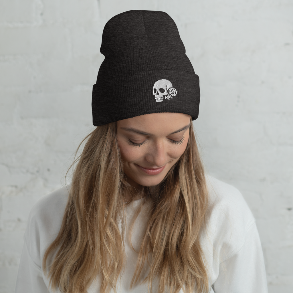 Woman wearing a black beanie with a skull and rose design against a light gray background