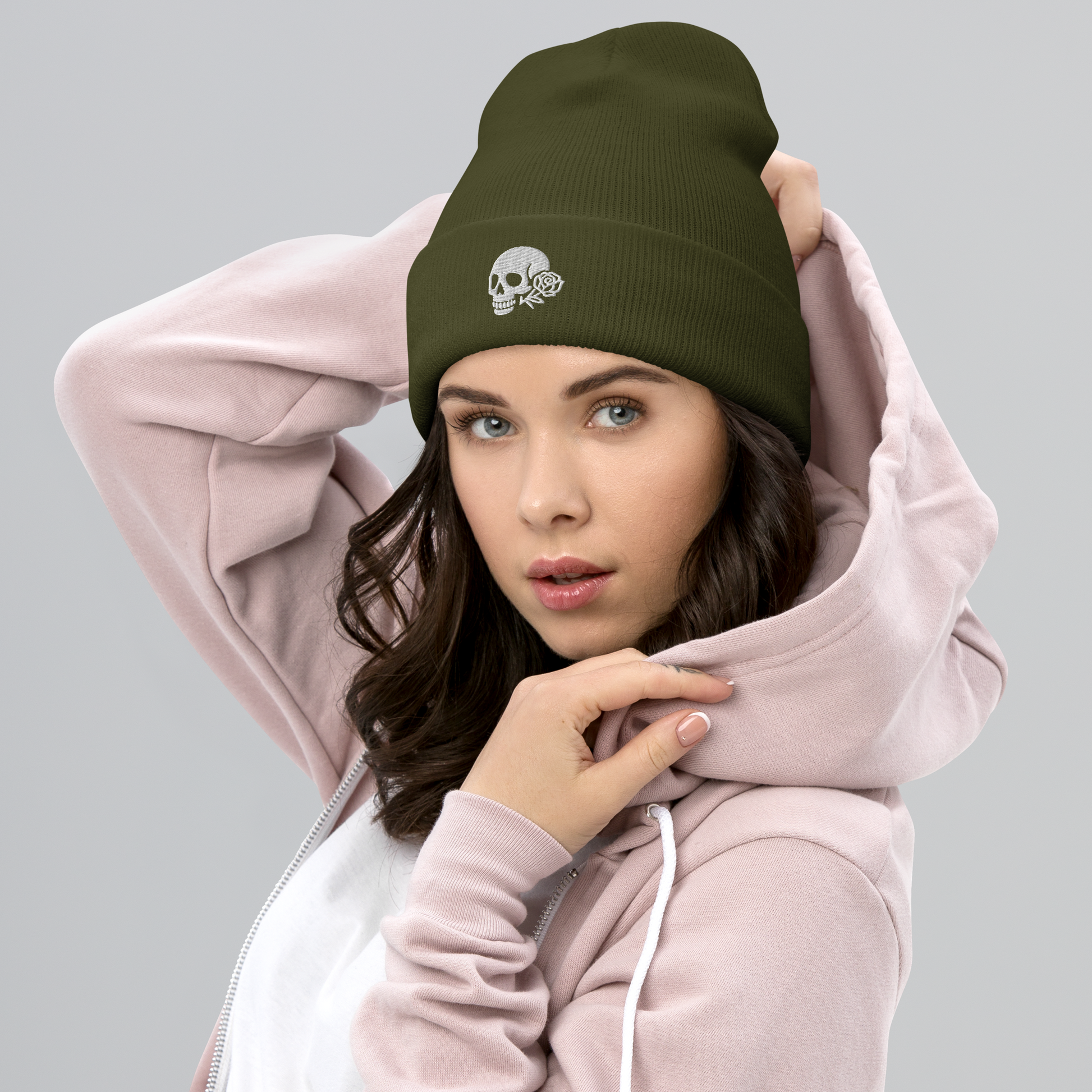 Woman wearing a pink hoodie and green beanie with skull design on a gray background