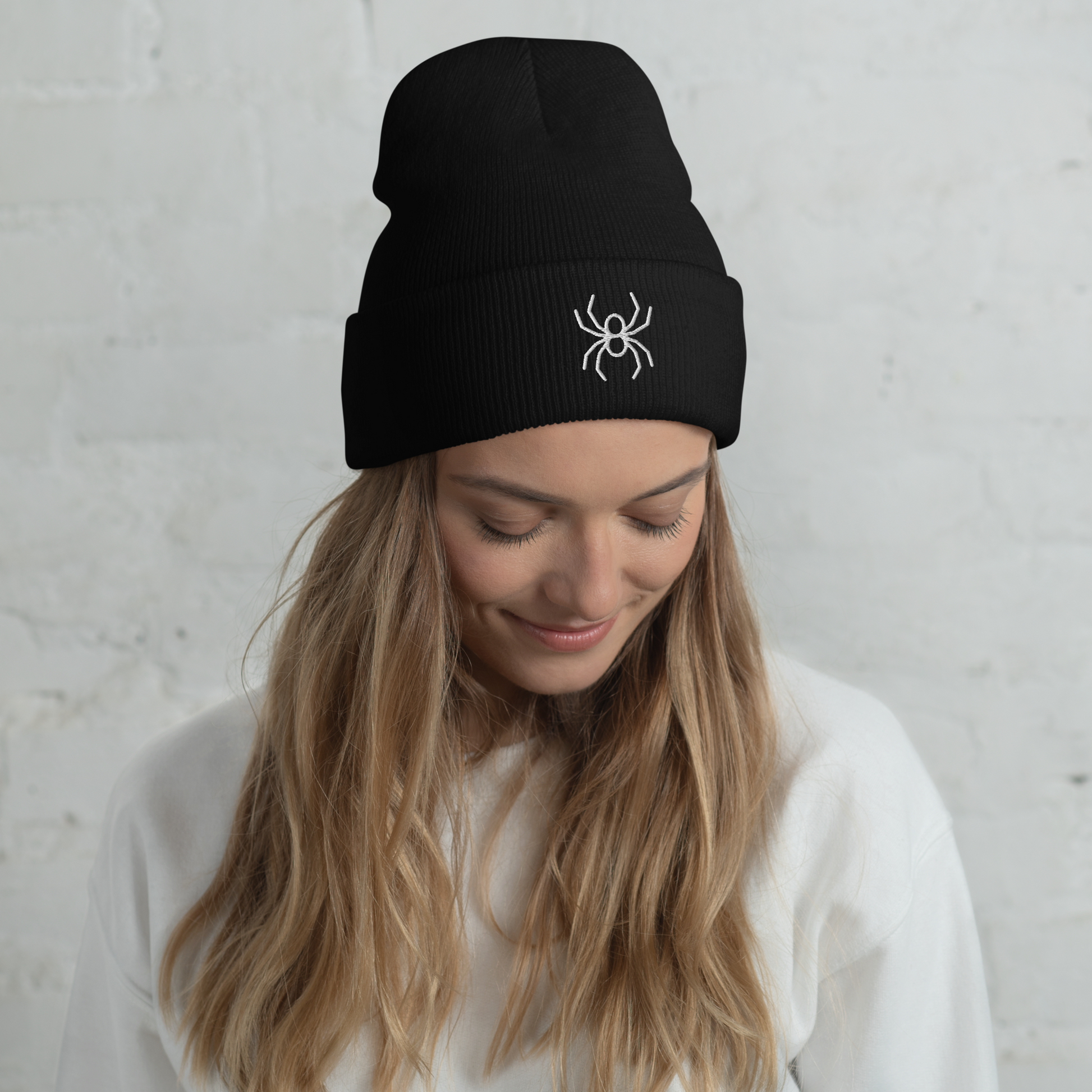 Person wearing a black beanie with a white spider emblem against a light gray background