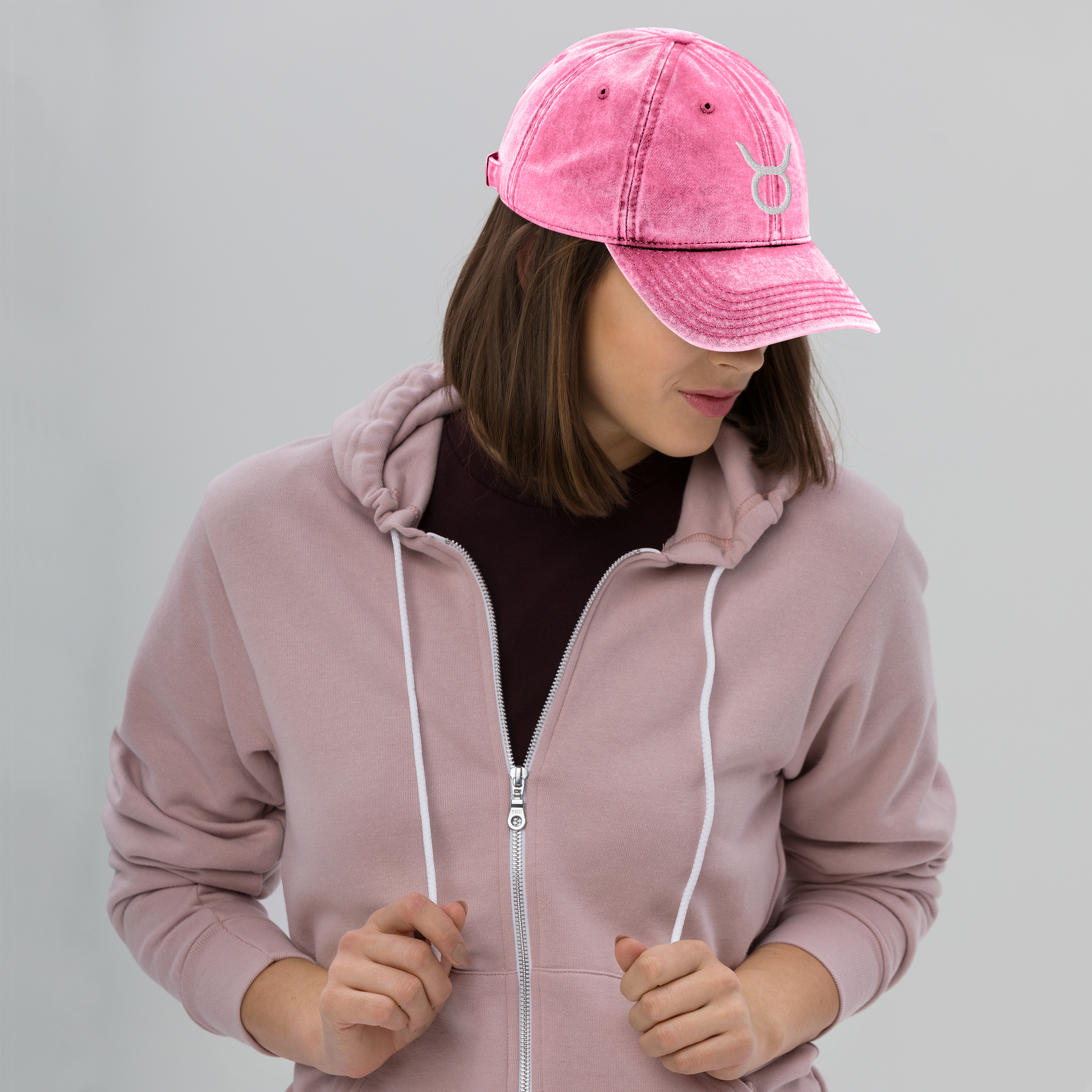Person wearing a pink hoodie and matching cap with a taurus symbol on a gray background