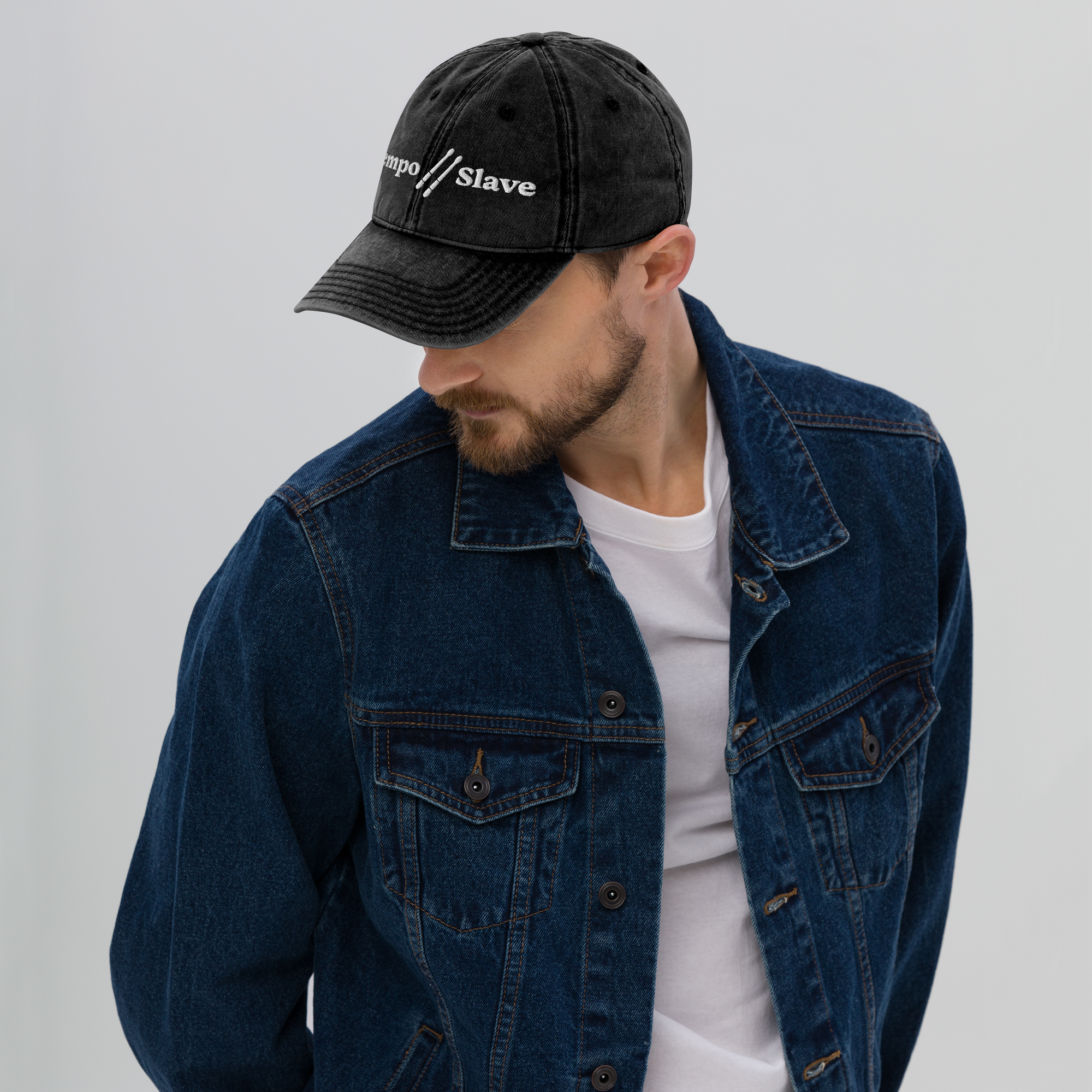 Man wearing a black cap with text and a blue denim jacket on a gray background