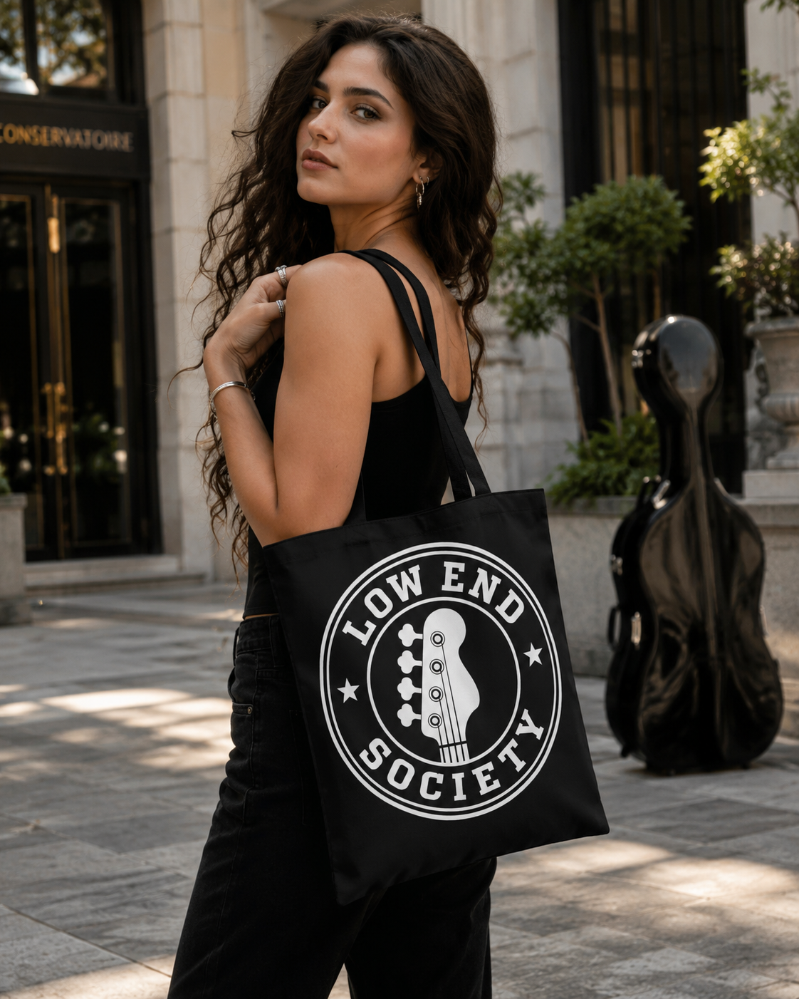 Woman holding a black tote bag with 'Low End Society' logo in an urban setting.