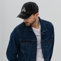 Man wearing a black cap with a logo and a blue denim jacket on a light gray background